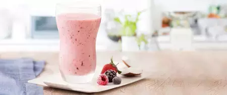 fotografía y tonos de rosa y blanco de un banco beige visto de frente, contiene un vaso transparente con la bebida de frutos rojos y al lado contiene frutos del bosque.