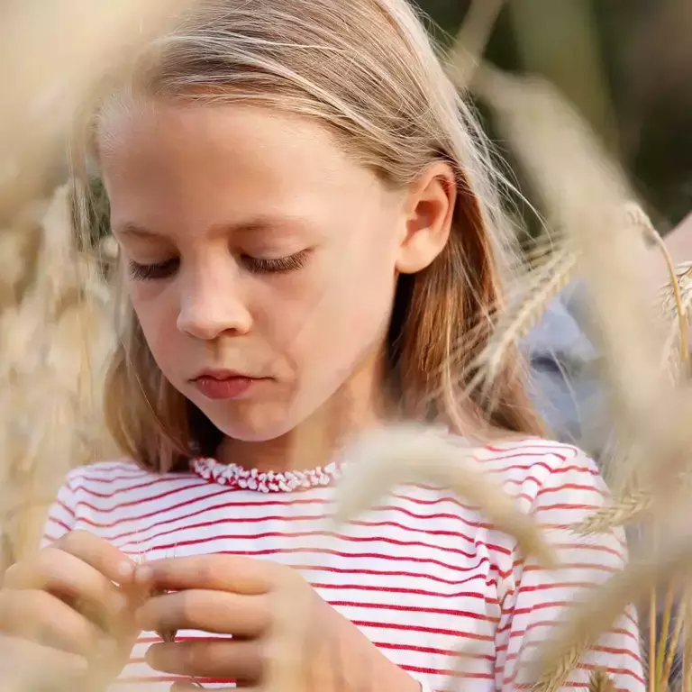 une petite fille dans un champ en train d’examiner du blé