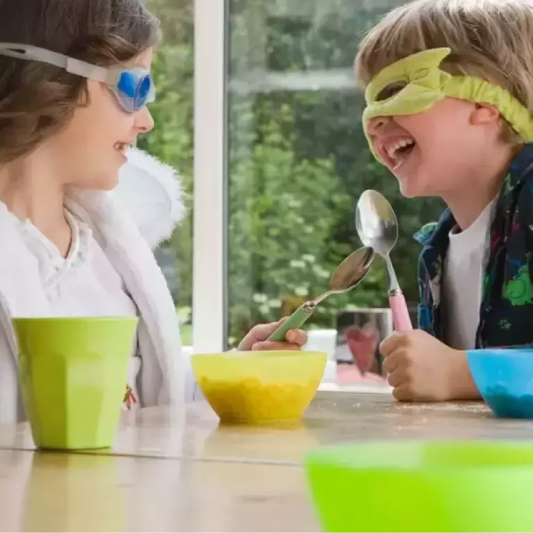 Egy fiú álarcban, egy lány úszószemüvegben ülnek a reggelizőasztalnál