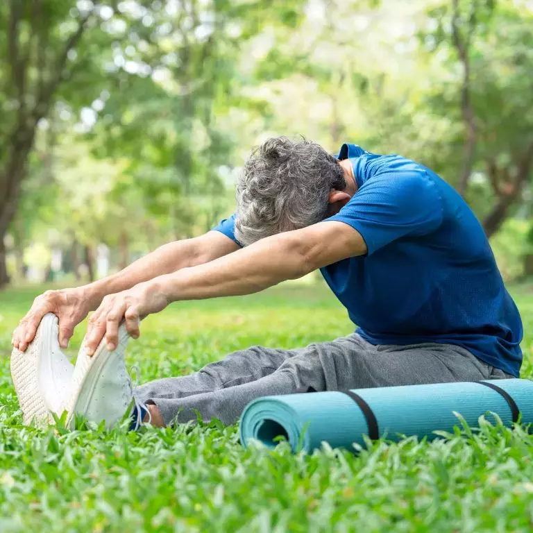 Man doing yoga in a blue tshirt and grey trousers