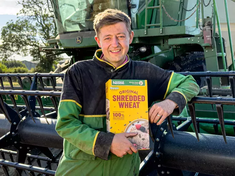 Farmer in front of a tractor holding a box of Shredded Wheat