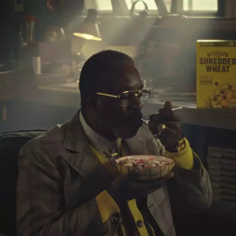 Rudy the inventor is eating a bowl of Shredded Wheat with the box alongside him.