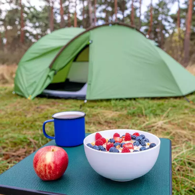 A green tent with a bowl of cornflakes, next to an apple and a cup of tea