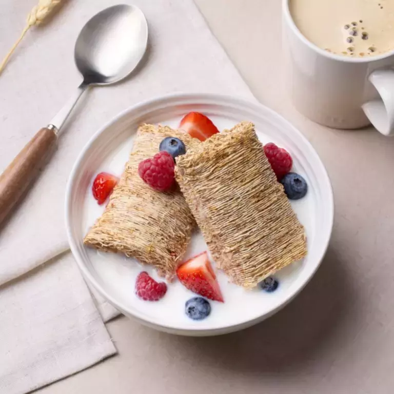 Shredded Wheat with berries and milk in white bowl, alongside a cup of coffee