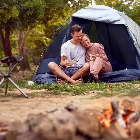 Man and a woman in a tent next to a fire with a bowl of cereal
